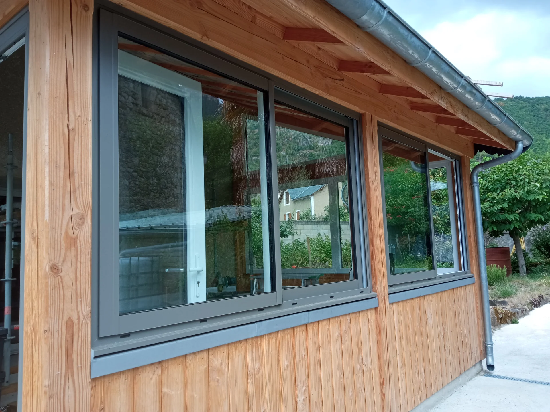 Vue longitudinale des fenêtres, du bardage bois et de la gouttière en zinc